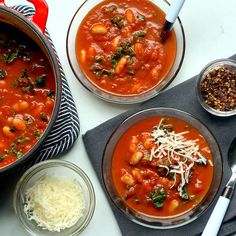 two bowls of soup with cheese and other food on the side, along with silver spoons