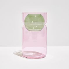 a pink vase sitting on top of a white table next to a green object in the middle