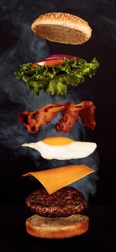 a hamburger flying through the air with bacon, lettuce and cheese