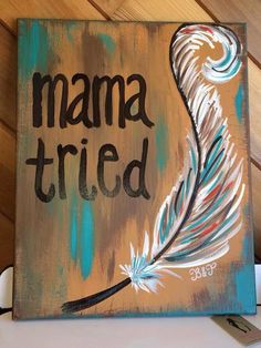 a painting with the words mama tried painted on it, and a feather resting on top