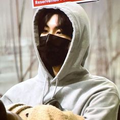 a man in a hoodie holding a teddy bear with a sign on his face