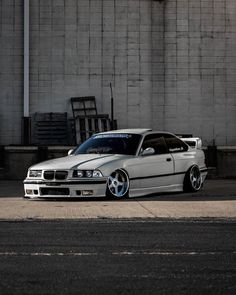 a white car parked in front of a building with its hood up and wheels down