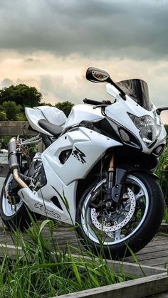 a white motorcycle parked on the side of a road next to tall grass and trees