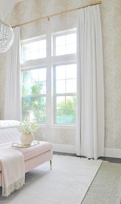 a white bed sitting next to a window in a room with curtains and rugs