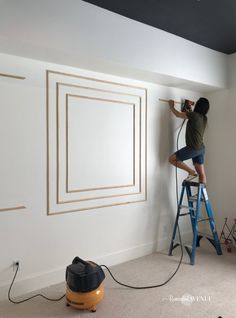 a person on a ladder painting the walls in a room with white paint and gold trim