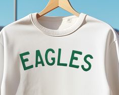 🦅💚 GO BIRDS! Amp up your game day look with our sleek Philadelphia Eagles Crewneck Sweater, designed especially for those who bleed green. A must-have for every Eagles enthusiast. Not just for game days, this contemporary sweater complements any casual ensemble, making you the highlight of every gathering. Whether you're embracing your inner Jason Kelce or giving a nod to Jalen Hurts, we've tailored your fashion-forward choice. From the pulsating streets of Philadelphia, Pennsylvania to buzzing tailgate celebrations, FLY EAGLES FLY. Make every Sunday a style statement! Note: Crafted for both men and women. Everyone deserves to look this good! 😉 👕🧢 𝗠𝗜𝗫-𝗡-𝗠𝗔𝗧𝗖𝗛 Looking for the ultimate game day outfit? Pair this with our matching sweatshirts, shirts, and other apparel to craft Casual Sports Tops With Letter Embroidery, White Team Spirit Sweatshirt With Embroidered Graphics, White Sweatshirt With Embroidered Graphics For Team Spirit, Sportswear Crew Neck Top With Embroidered Logo, White Sporty Sweatshirt With Letter Embroidery, Sporty White Sweatshirt With Letter Embroidery, College Sports Season Tops With Letter Embroidery, Sportswear Tops With Embroidered Logo For Sports Season, Sportswear Tops With Embroidered Logo And Crew Neck