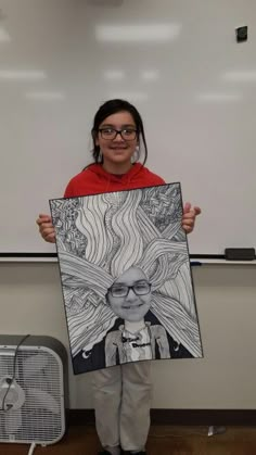 a woman holding up a drawing in front of a whiteboard with a black and white image on it