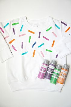 three cans of sprinkles are sitting next to a white sweater with colorful sprinkles on it