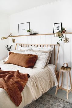 a bed with white sheets and brown pillows in a bedroom next to a wooden table