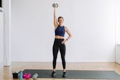 a woman is doing exercises with dumbbells on a mat in an empty room