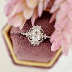 an engagement ring sitting on top of a purple velvet box with pink flowers in the background