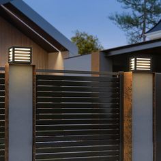 two lights on the side of a building next to a fence and gate with a house in the background