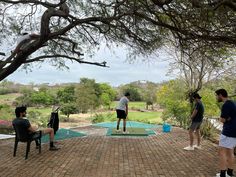 three people standing on top of a brick patio next to a tree and pool area