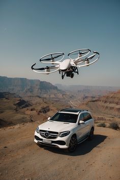 a white car parked on top of a dirt road next to a remote control helicopter