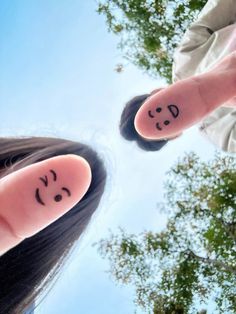 two people with faces drawn on their fingers are looking up at the sky and trees