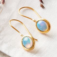 A beautiful iridescent fiery white rainbow opal simple and stylish drop earring set in 18 carat gold plated on sterling silver.  These minimalist simple opal drops are the perfect everyday earring. The rainbow effect is so enchanting changing from white to blue and orange as you move in a magical way. Handmade using the finest materials and natural opal personally sourced around the globe! All the materials I use are real Sterling Silver and 18 carat gold. I do not use inferior metals such as Gold fill or Brass Gold plated! Ideal for a friend's birthday, a bride's outfit, or for yourself. Opal is the birthstone for anyone born in October.  This is said to be an emotional gemstone, which reflects the mood of the wearer. These earrings measure 3cm long and 1cm wide. These earrings are also a Gold Opal Cabochon Earrings, Oval Opal Earrings In Yellow Gold, Yellow Gold Oval Opal Earrings, Elegant Ethiopian Opal Earrings As Gift, Gold Oval Earrings, London Blue Topaz Necklace, Opal Birthstone, Blue Topaz Jewelry, Rainbow Opal