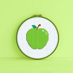 an apple cross stitched into a hoop on a green wall with a wooden frame