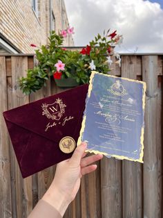 a person holding up an envelope with a wedding card in front of a wooden fence