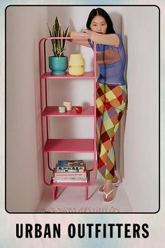 a woman leaning against a pink shelf with potted plants on it and the caption urban outfitters