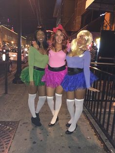 three women dressed up in costumes posing for a photo on the side walk at night