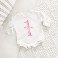 This first birthday design includes a watercolor pink 1 and personalized name, and is available in 8 different product types. The design is printed on 100% cotton on either a short sleeve bodysuit, long sleeve bodysuit, sweatshirt romper, sleeper, or toddler sweatshirt, long sleeve, or short sleeve. This piece is a sturdy material, cozy soft and perfect for staying cuddly. Perfect for your babe's bday celebration. Sizing: long and short sleeves: true to size sweatshirt romper and sweatshirt: oversized sleeper: fits large sweatshirt: slightly oversized but more true to size This product is handprinted using nontoxic, water-based inks on a cotton sweatshirt material romper with three snaps. This item comes in the following infant sizes  6-12 months 12-18 months 18/24 months 2T Gentle cycle o Personalized Pink Top For First Birthday, Personalized Pink Tops For First Birthday, Custom Pink Tops For First Birthday, Simple Birthday Outfit, Birthday Outfit Pink, Birthday Romper, Bday Celebration, Sweatshirt Romper, 1st Birthday Outfit