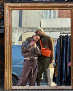 two people taking a selfie in front of a mirror with clothes hanging on the rack