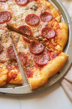 a pepperoni pizza cut into four slices on a pan with one slice taken out