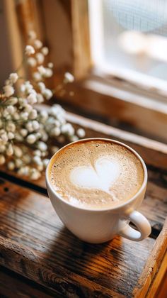 a cup of coffee sitting on top of a wooden table next to a vase with flowers