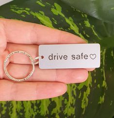 a hand holding a keychain with the words drive safe on it and a watermelon plant in the background