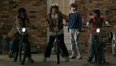 four young men standing next to each other on bikes in front of a brick building