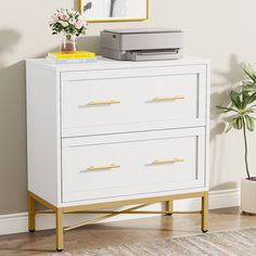 a white dresser with gold handles and drawers in a room next to a potted plant