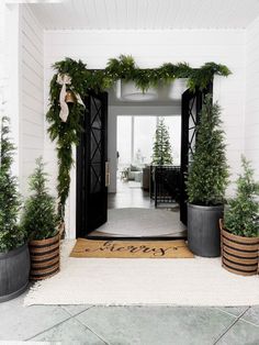 an entry way decorated for christmas with evergreen garland and potted trees