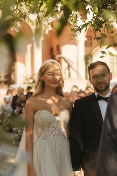 a bride and groom standing under a tree in front of an outdoor ceremony with people watching