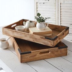 two wooden trays with tea cups and books on them sitting on a white table