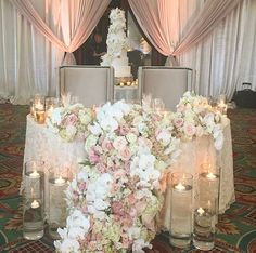 a table topped with lots of white and pink flowers next to tall vases filled with candles