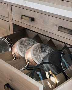 an open drawer with several pots and pans in it on top of a counter