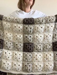 a woman is holding up a crocheted blanket with squares on the bottom and sides