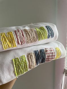 two white towels with the word mom embroidered on them are being held by someone's hand