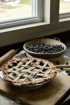 two pies sitting on top of a wooden cutting board next to each other near a window