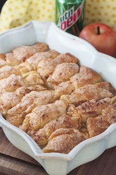 an apple pie sitting on top of a wooden cutting board next to some apples and a can of soda