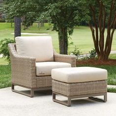 a wicker chair and foot stool in front of a tree on a patio area