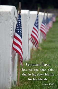 rows of american flags lined up on the side of a stone wall in a cemetery