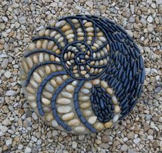 a decorative rock sitting on top of a gravel covered ground with rocks and pebbles in the shape of a spiral