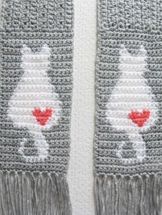 two crocheted scarfs with red hearts on them, one is gray and the other is white