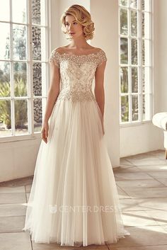 a woman in a white wedding dress standing on a tile floor with windows behind her