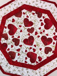 a red and white quilted table topper with hearts on the center, surrounded by vines