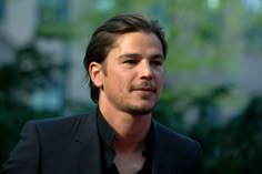 a close up of a person wearing a suit and tie with trees in the background