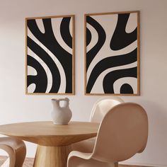 two black and white paintings hanging on the wall next to a dining room table with chairs