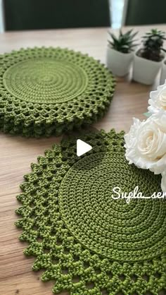 two crocheted placemats with white flowers on the top and one is green