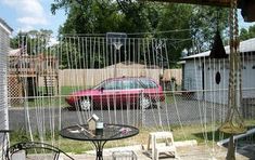 a red car is parked behind a chain link fence in front of a backyard table and chairs